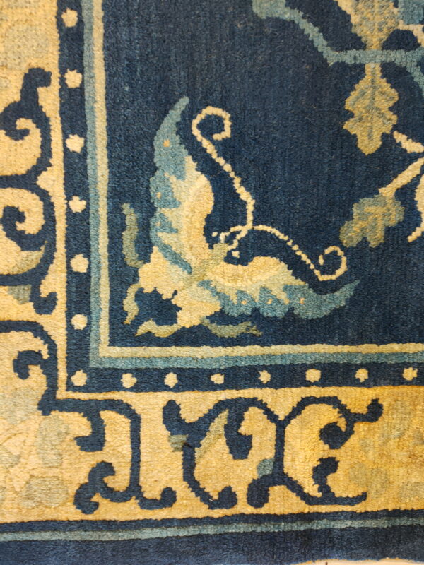 Deep blue rug corner with golden yellow and aqua botanical patterns on a visible medium pile.