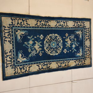 Low pile navy rug with a complex tan border and central floral medallion on light floor tiles.