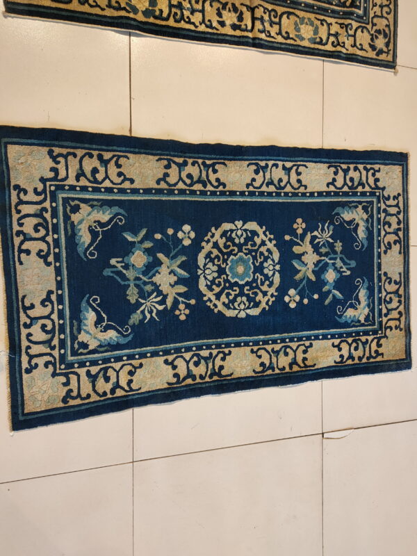 Low pile navy rug with a complex tan border and central floral medallion on light floor tiles.