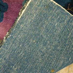 Low-pile purple floral rug is folded, revealing its dense woven blue backing resting on wood flooring.