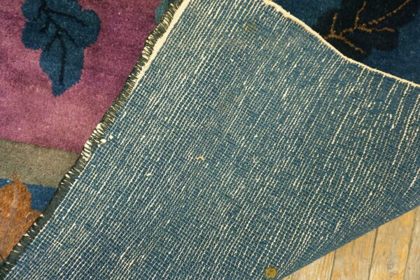 Low-pile purple floral rug is folded, revealing its dense woven blue backing resting on wood flooring.