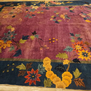 Medium pile rug with a plum field and navy border featuring a complex multi-color botanical pattern.