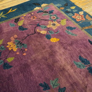 Overlapping purple and deep blue rugs feature large stylized floral designs on a rustic light wood floor.