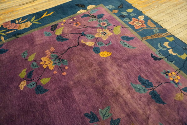 Overlapping purple and deep blue rugs feature large stylized floral designs on a rustic light wood floor.