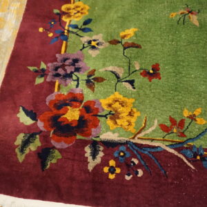 Close-up of a high-pile floral rug with a lime green field and deep burgundy border on distressed wood.