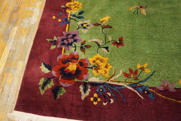 Close-up of a high-pile floral rug with a lime green field and deep burgundy border on distressed wood.