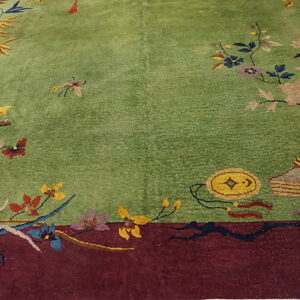 Green rug with a maroon border featuring colorful flowers, bamboo, and decorative objects.