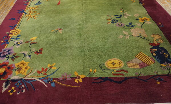 Green rug with a maroon border featuring colorful flowers, bamboo, and decorative objects.