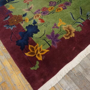 High-pile rug features a green field, burgundy border, and colorful floral pattern on distressed wood flooring.