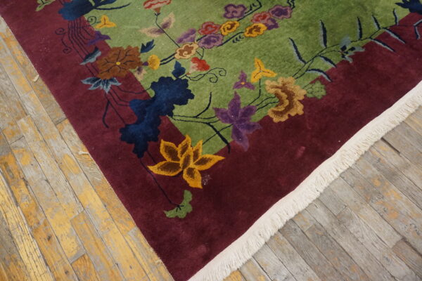 High-pile rug features a green field, burgundy border, and colorful floral pattern on distressed wood flooring.