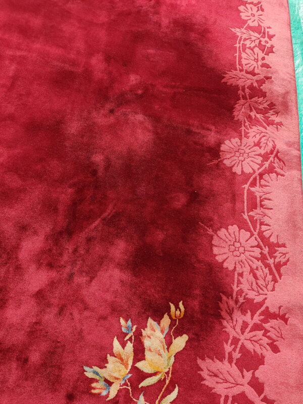 Velvety deep red rug featuring a tone-on-tone pink floral border and multicolored accent flowers.