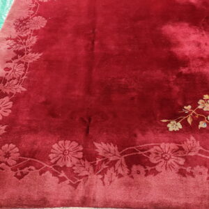 A crimson plush rug features a carved tone-on-tone floral border and a multicolored yellow and blue corner motif.