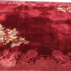 A shiny, deep red plush rug features carved floral borders and colorful stylized flower arrangements in the corners.