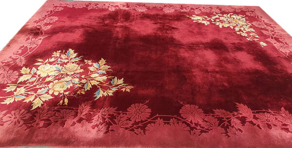 A shiny, deep red plush rug features carved floral borders and colorful stylized flower arrangements in the corners.