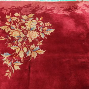 Deep red plush rug featuring a large multicolored floral bouquet and a patterned tone-on-tone border.
