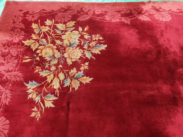 Deep red plush rug featuring a large multicolored floral bouquet and a patterned tone-on-tone border.