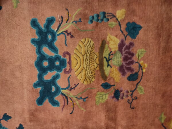 Muted pink rug detail showing stylized floral pattern in teal, bright yellow, plum, and green.