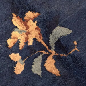 Textured dark blue pile rug featuring a botanical motif in tan, sienna, and pale gray colors.