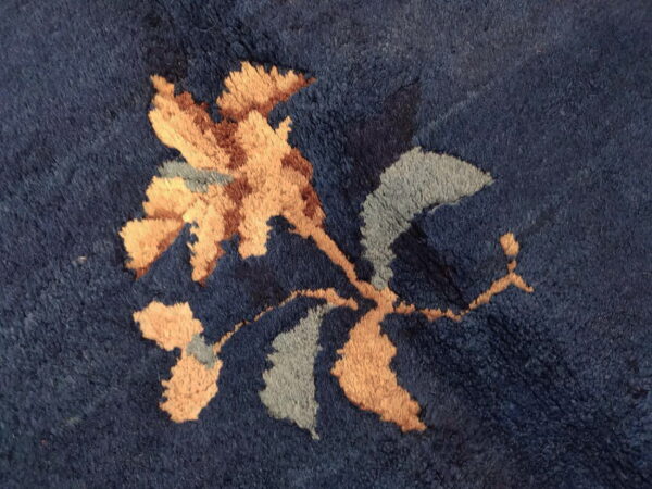 Textured dark blue pile rug featuring a botanical motif in tan, sienna, and pale gray colors.