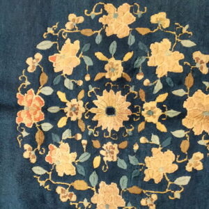 Detailed view of a deep blue rug showing a circular floral medallion in gold, pale blue, and rust.