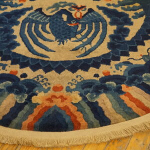 Blue bird motif on a high-pile tan rug, featuring orange borders and long beige fringe on wood.