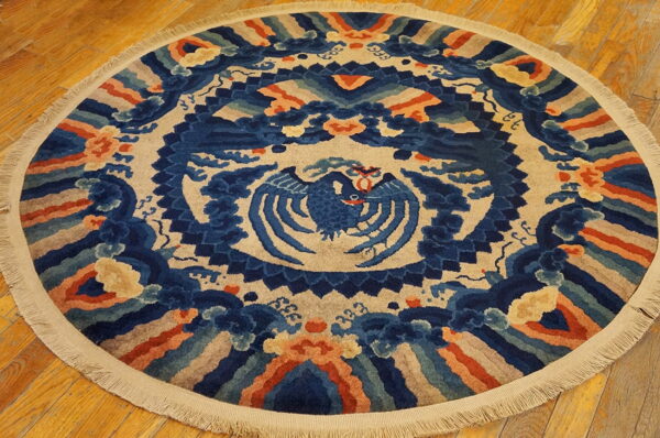 High-pile round rug in blue, beige, and terracotta featuring an ornate stylized bird motif on wood flooring.