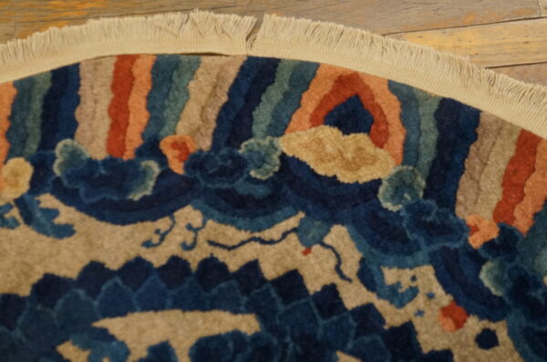 Round rug detail showing plush pile, navy and tan stylized waves, and multicolored striped borders on wood floor.