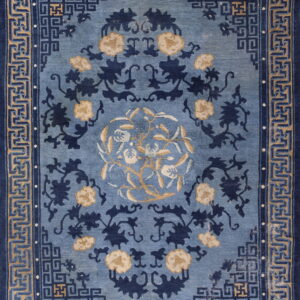 Slate blue rug with navy and tan botanical patterns bordered by complex geometric fretwork designs.