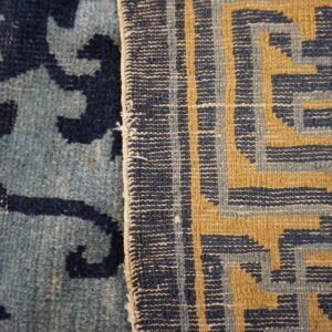Detailed view of two contrasting rugs: one low-pile blue botanical, one flatwoven blue and gold geometric.