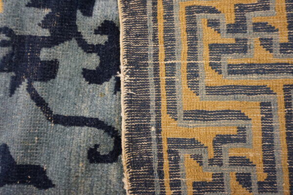 Detailed view of two contrasting rugs: one low-pile blue botanical, one flatwoven blue and gold geometric.