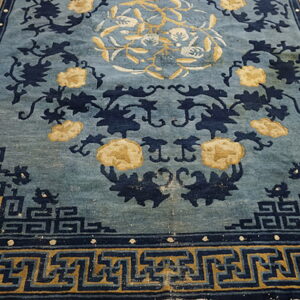 Blue rug with yellow floral motifs and dark blue geometric borders rests on wood planks.