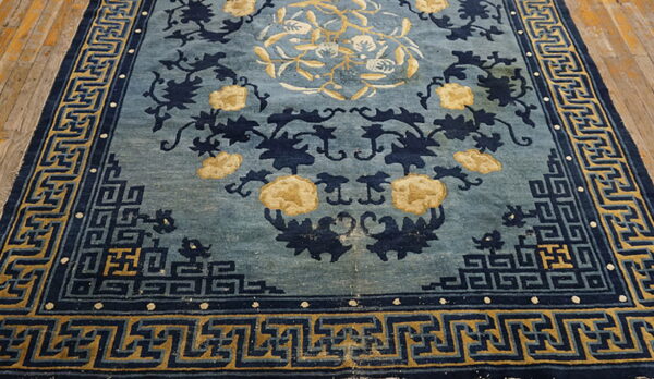 Blue rug with yellow floral motifs and dark blue geometric borders rests on wood planks.