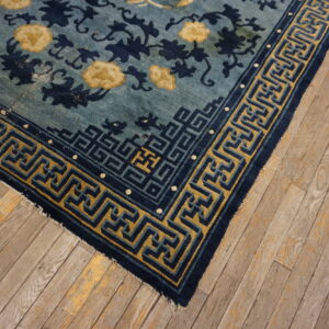 Blue floral rug with navy and mustard yellow key border detail shown on distressed wood planks.