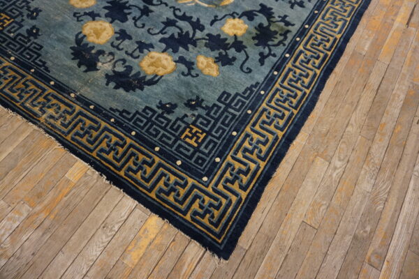 Blue floral rug with navy and mustard yellow key border detail shown on distressed wood planks.