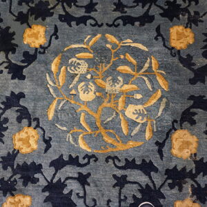 Blue rug with a gold floral central medallion, navy vines, and a yellow geometric border.