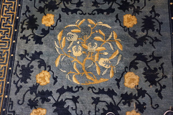 Blue rug with a gold floral central medallion, navy vines, and a yellow geometric border.