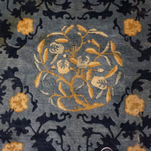 Close up of a faded slate blue rug patterned with dark indigo and golden yellow floral designs.