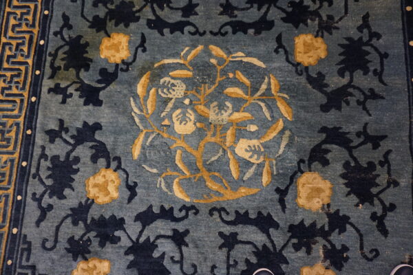Close up of a faded slate blue rug patterned with dark indigo and golden yellow floral designs.