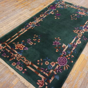 Dark green rug with a colorful floral and tan geometric border is placed on light distressed hardwood flooring.