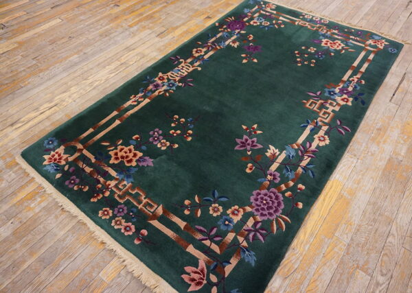 Dark green rug with a colorful floral and tan geometric border is placed on light distressed hardwood flooring.