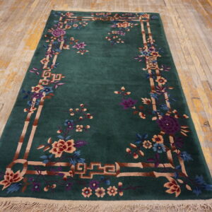Green rug with elaborate multicolor floral and bamboo border pattern displayed on distressed wood floors.