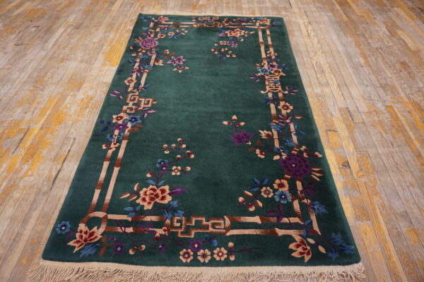 Green rug with elaborate multicolor floral and bamboo border pattern displayed on distressed wood floors.