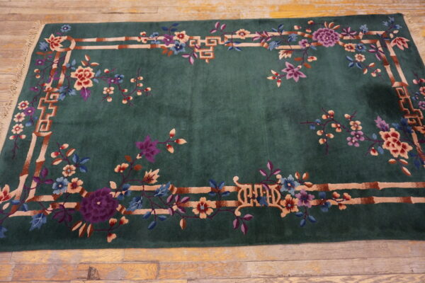 Emerald green low-pile rug with plum, pink, and blue florals bordered by bamboo fretwork on wood flooring.