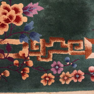 Close-up of a plush green rug featuring tan and brown fretwork with large floral elements in red, peach, and purple.