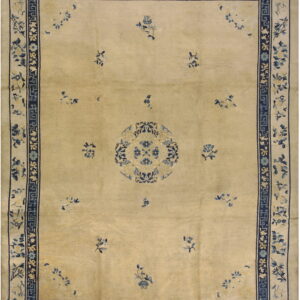 Tan low-pile rug with dark blue borders, central medallion, and scattered light blue floral designs.