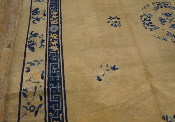 Beige rug with deep blue, light blue, and yellow floral patterns and a geometric border on wood floors.