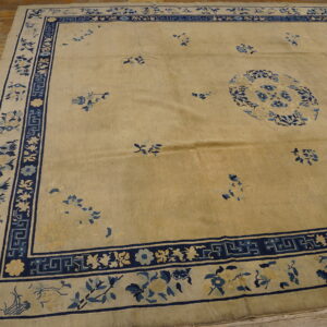 Low-pile tan rug with blue floral medallion and ornate border on distressed wood flooring.