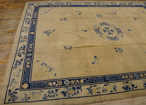 Low-pile tan rug with blue floral medallion and ornate border on distressed wood flooring.