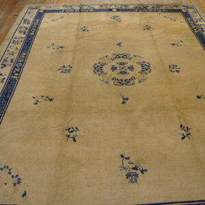 Tan field rug with a central blue floral medallion and wide blue decorative borders on wood planks.