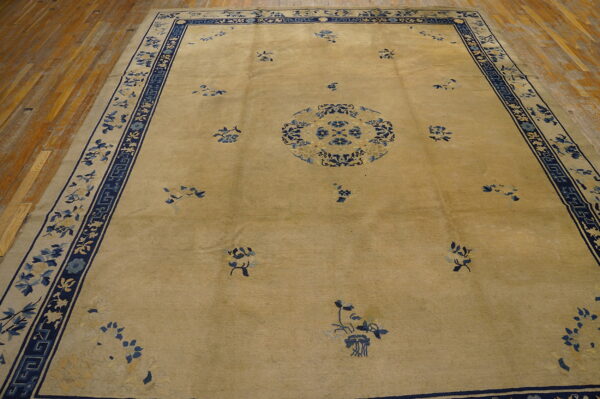 Tan field rug with a central blue floral medallion and wide blue decorative borders on wood planks.
